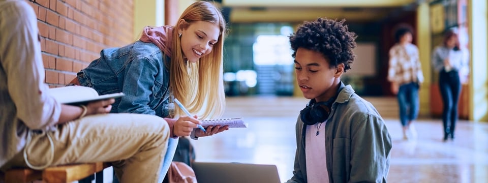 teenager using laptop while studying with his friends in high school hallway.