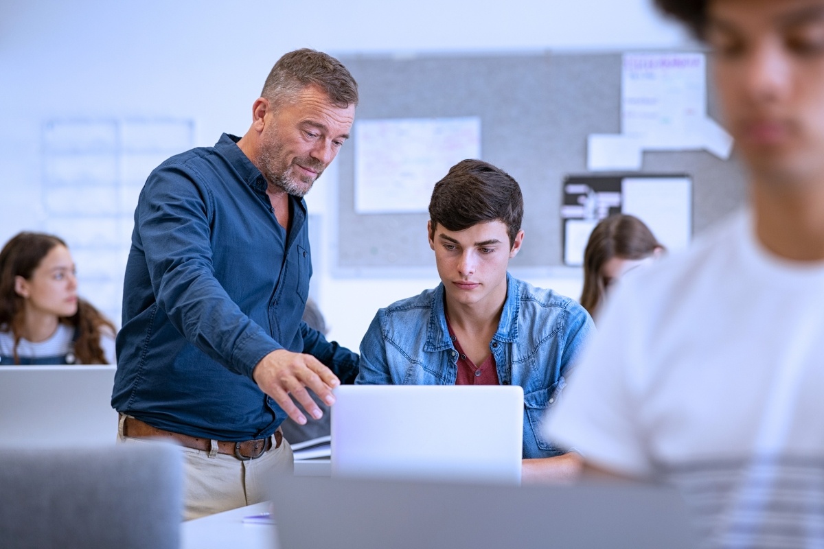  lecturer helping high school teen with laptop during lecture.