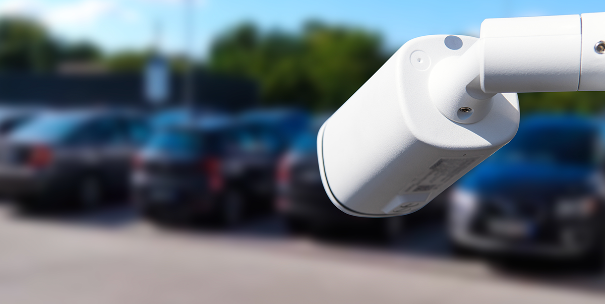 An image of a school campus parking lot, featuring a high-tech security camera mounted on a pole, actively monitoring vehicles entering and exiting the area. 