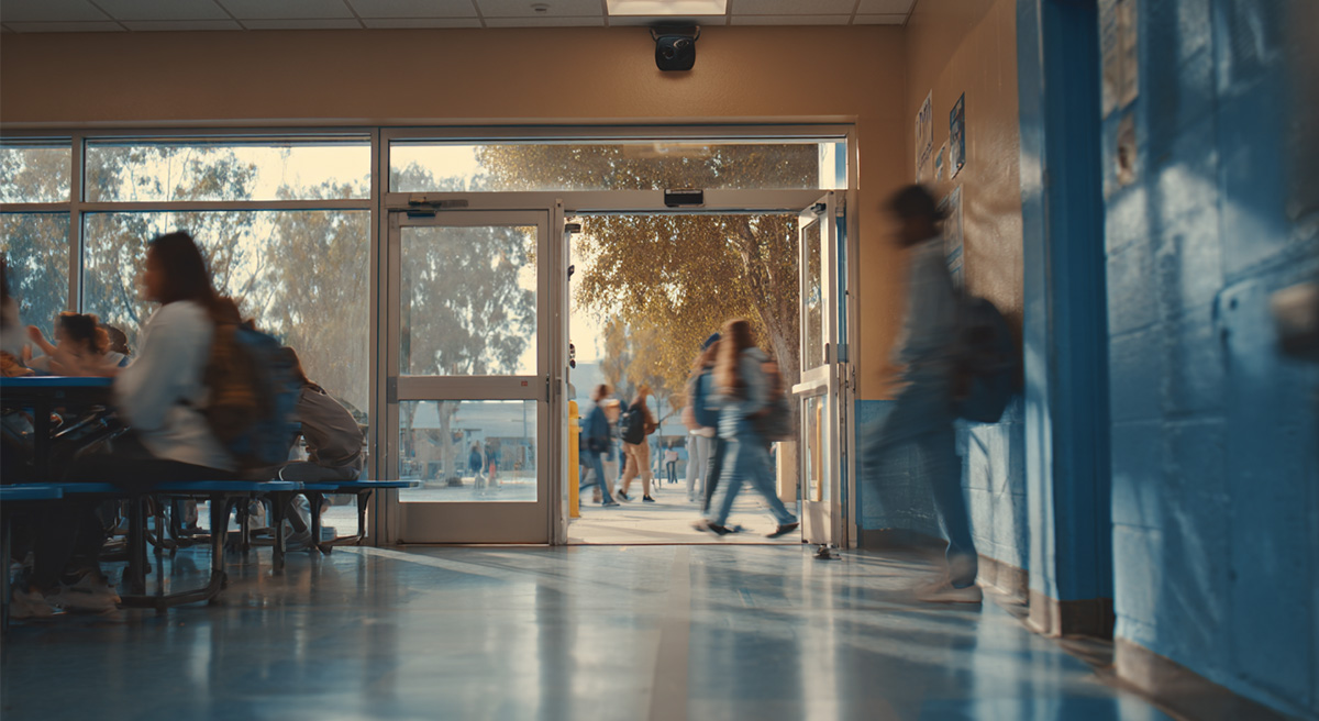 Morning scene at a California middle school cafeteria entrance. A small scuffle between students is happening near the doors, with motion blur to suggest fast action.